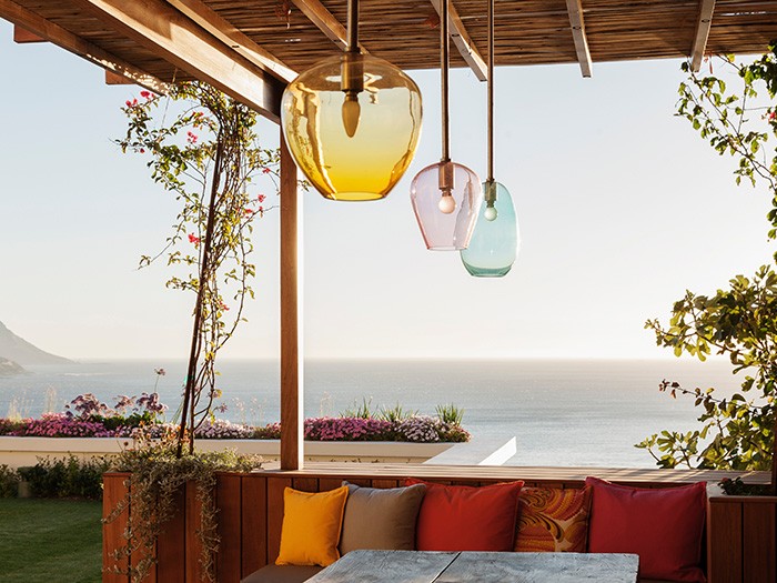 elevated patio with wooden deck seating and accent colorful pillows with overhanging light fixtures in yellow, pink and blue. 